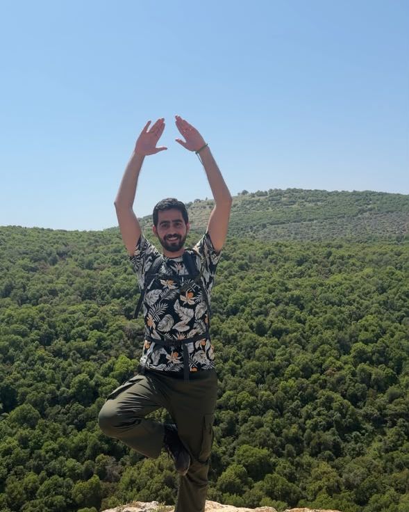 Fares in tree pose on a cliff edge over the forest