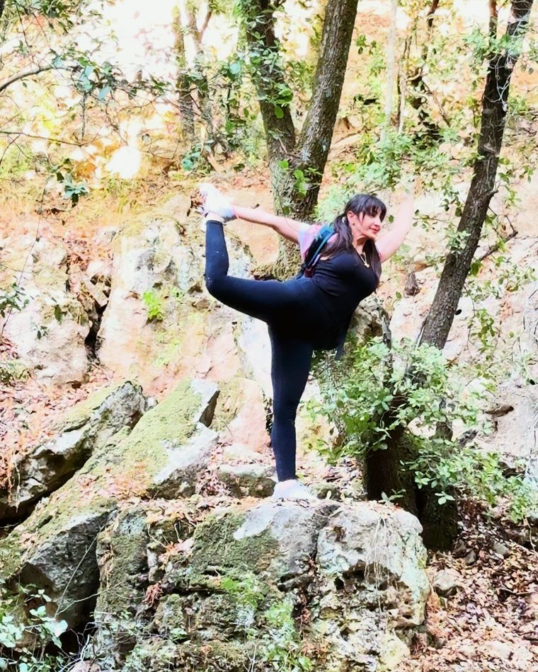Sahar smiling in dancer pose on a mossy rock in the forest
