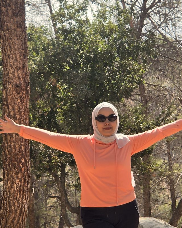 Afaf with her arms open between two pines