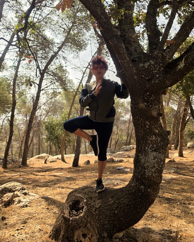 Wafaa crouched by an oak, making a peace sign