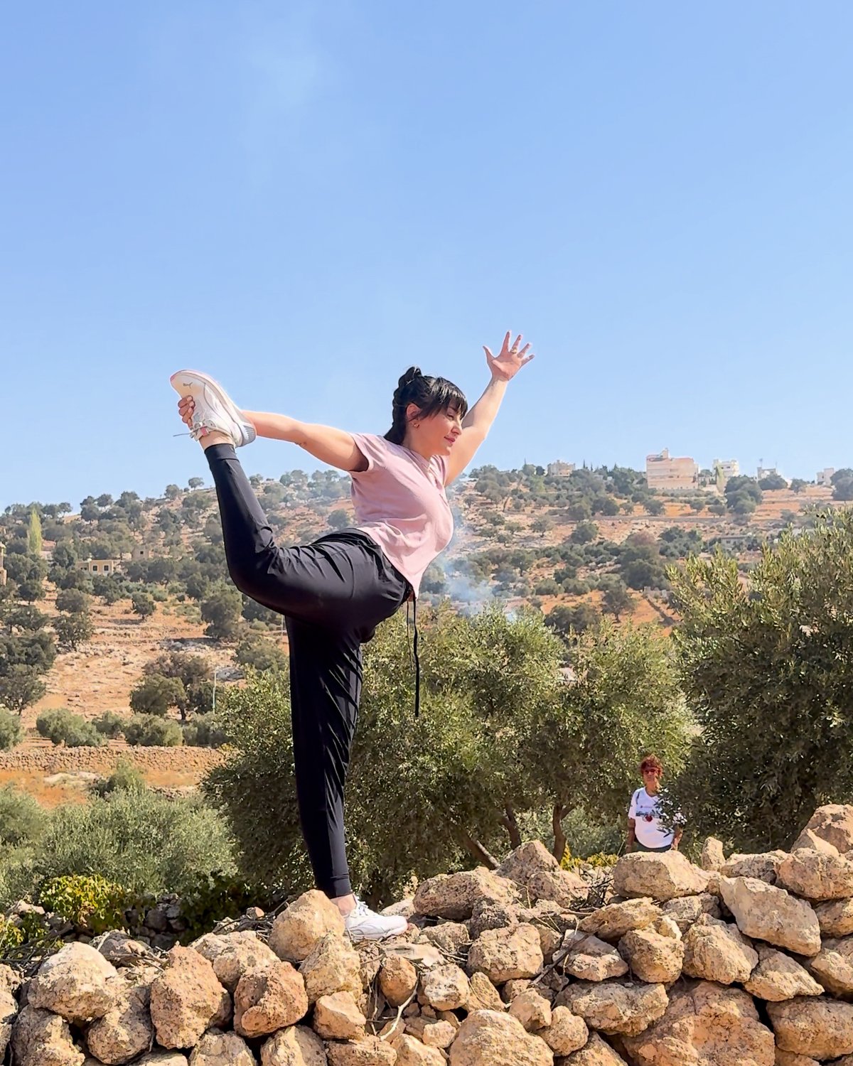 Sahar in dancer pose on a stone wall under a blue sky, Al Hadaba